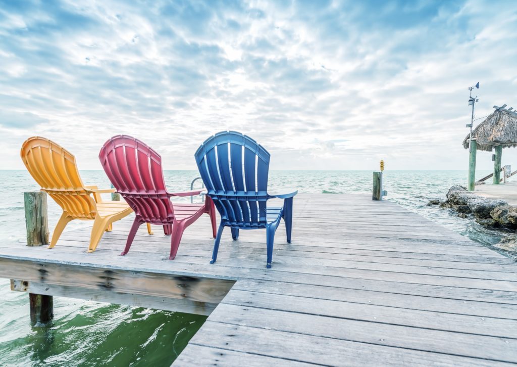 Three empty beach chairs sitting on a dock facing the water